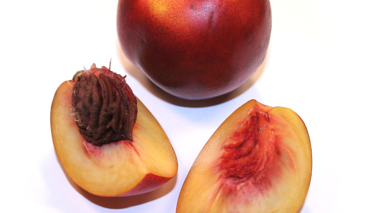 Whole nectarine beside two halved nectarines showing the pit